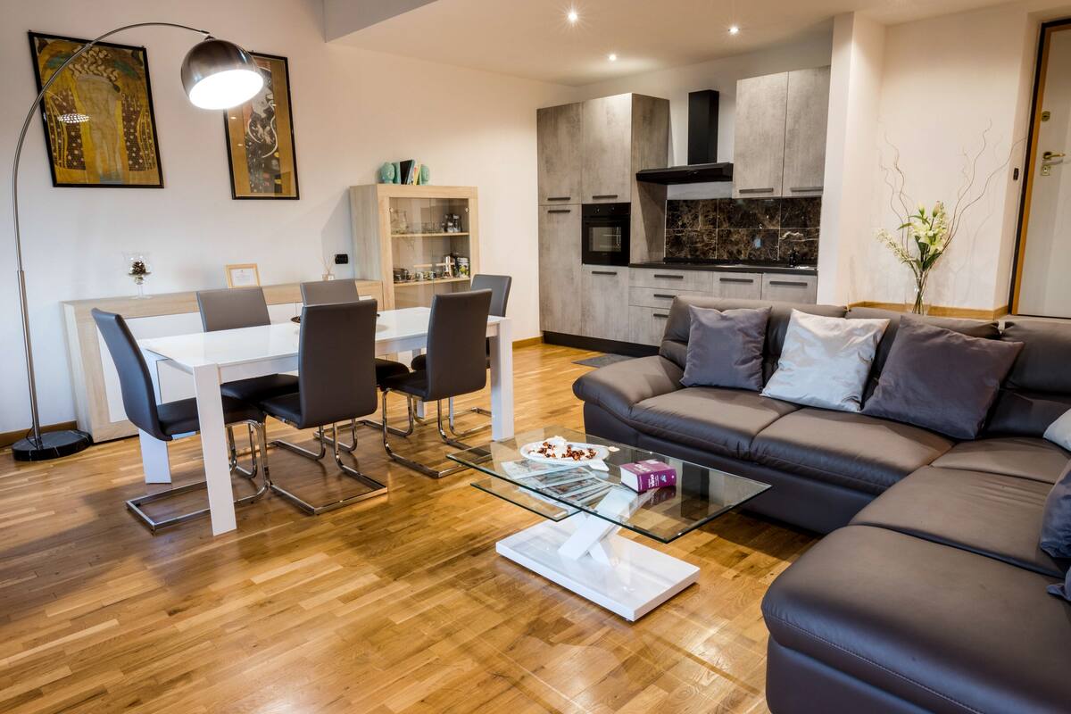 A modern living room with a glass coffee table, a gray sofa, and a dining area with a white table and chairs.