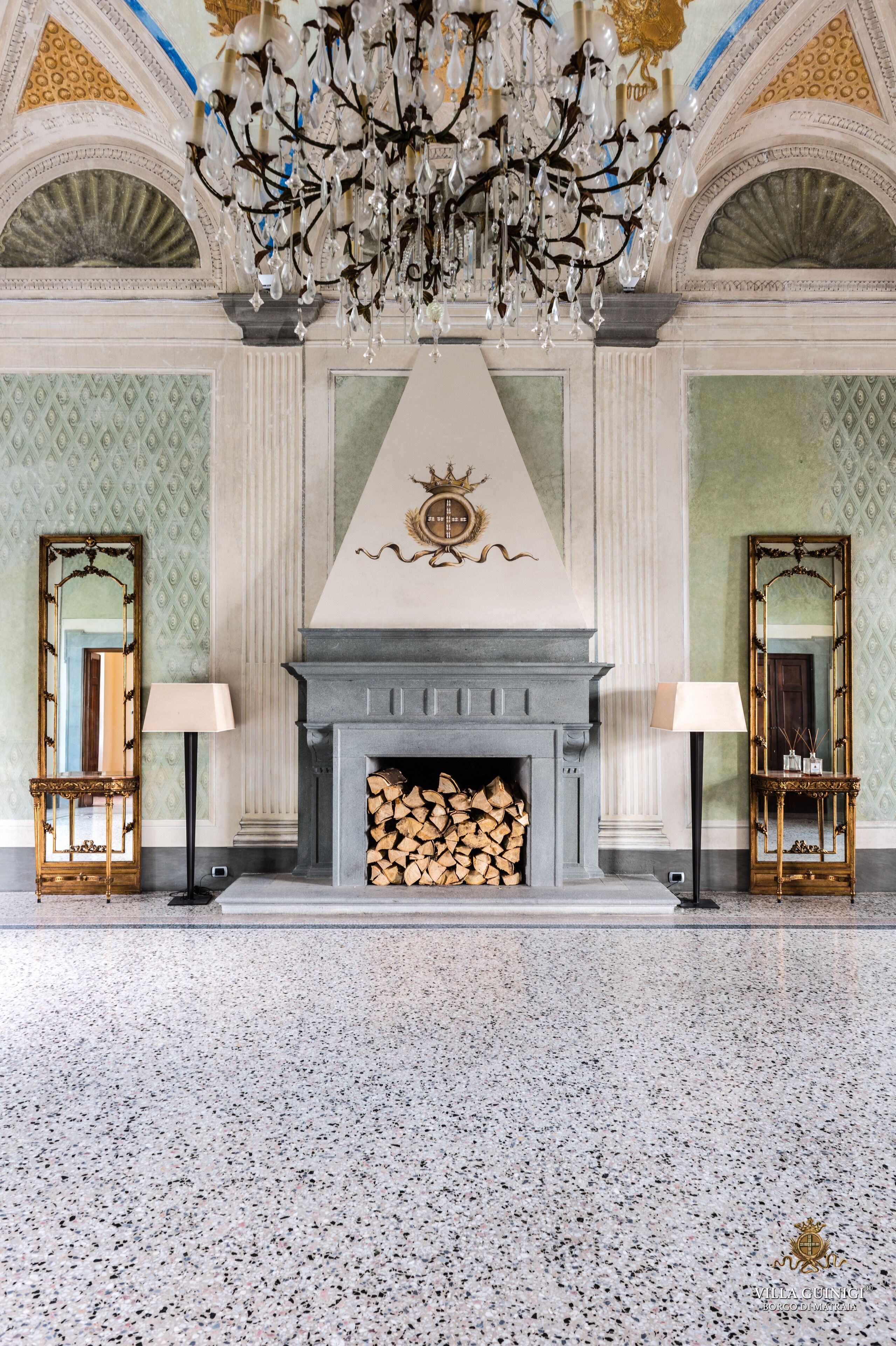 A grand lobby with a fireplace, chandeliers, and ornate mirrors.