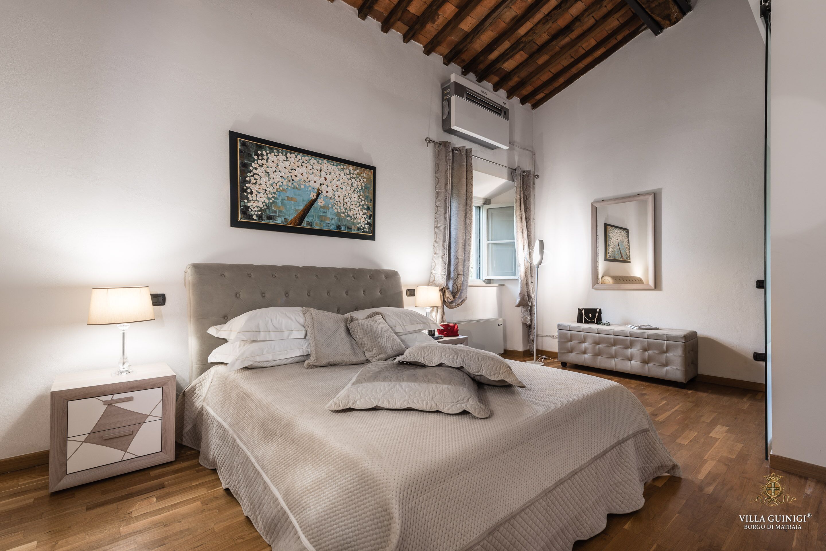 A bedroom with a large bed, a nightstand, a bedside table, a mirror, and a painting on the wall.