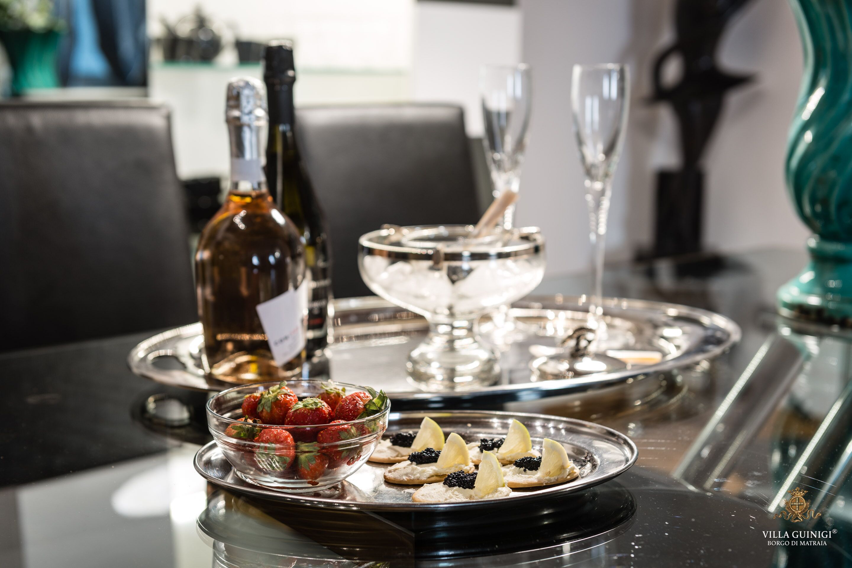 Une table à manger avec une bouteille de vin, un saladier de fraises et un plateau de pâtisseries.