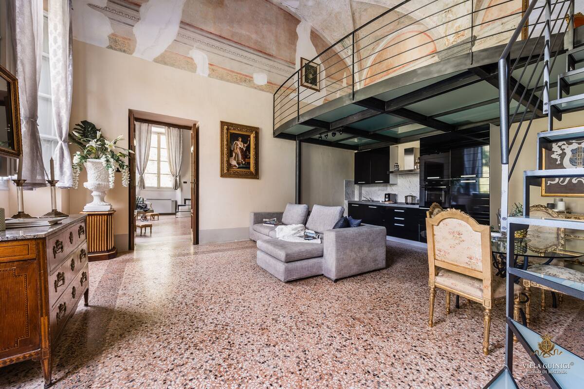 A spacious living area with a grey sofa, a wooden cabinet, and a dining table. A staircase leads to an upper level.