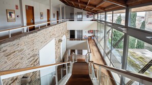 A multi-level interior with a wooden staircase, stone walls, and large windows offering views of the outside.