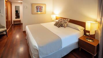 Een hotelkamer met een groot bed, bedlampjes, een houten nachtkastje, een bankje en een spiegel.