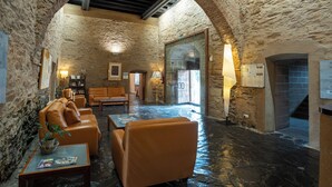 A stone-walled room with leather sofas, a coffee table, and a lamp.