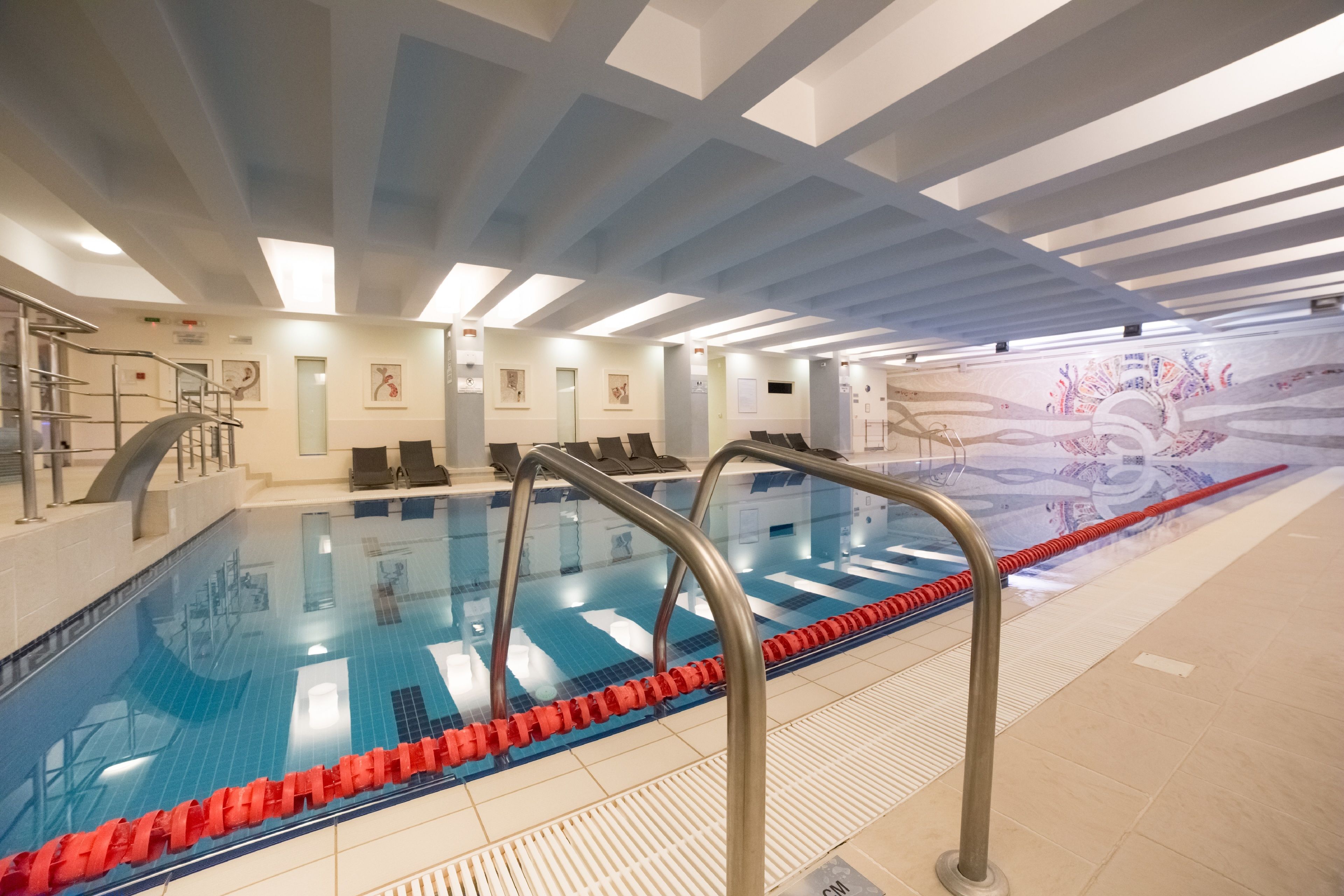 Una piscina interior con carriles delimitados, una plataforma de salto y un mural en la pared.