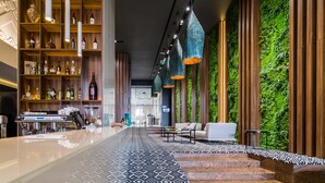 A modern bar area with a long counter, shelves with bottles, and hanging lights.