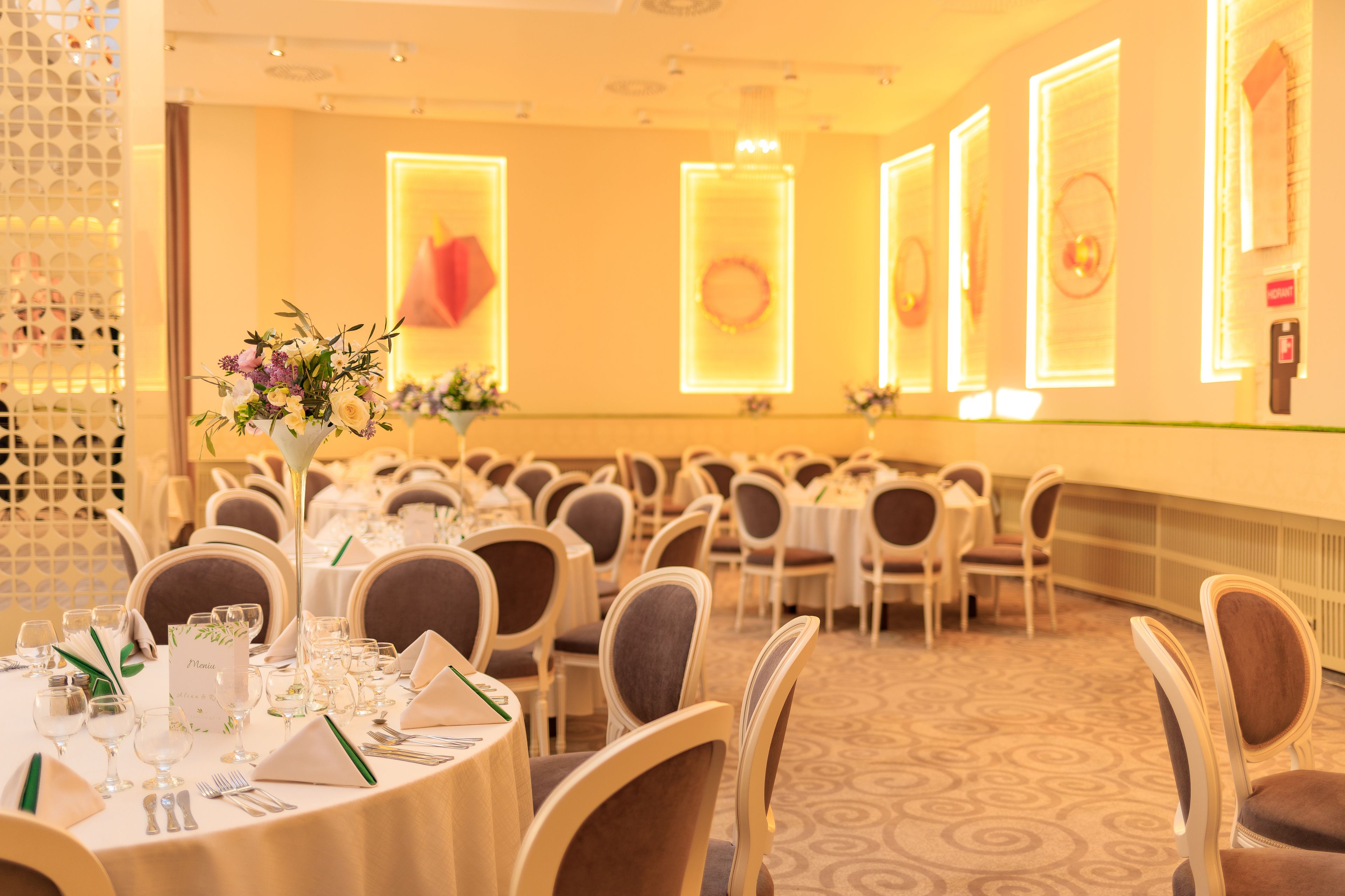 Een feestzaal met ronde tafels, stoelen en bloemdecoraties.
