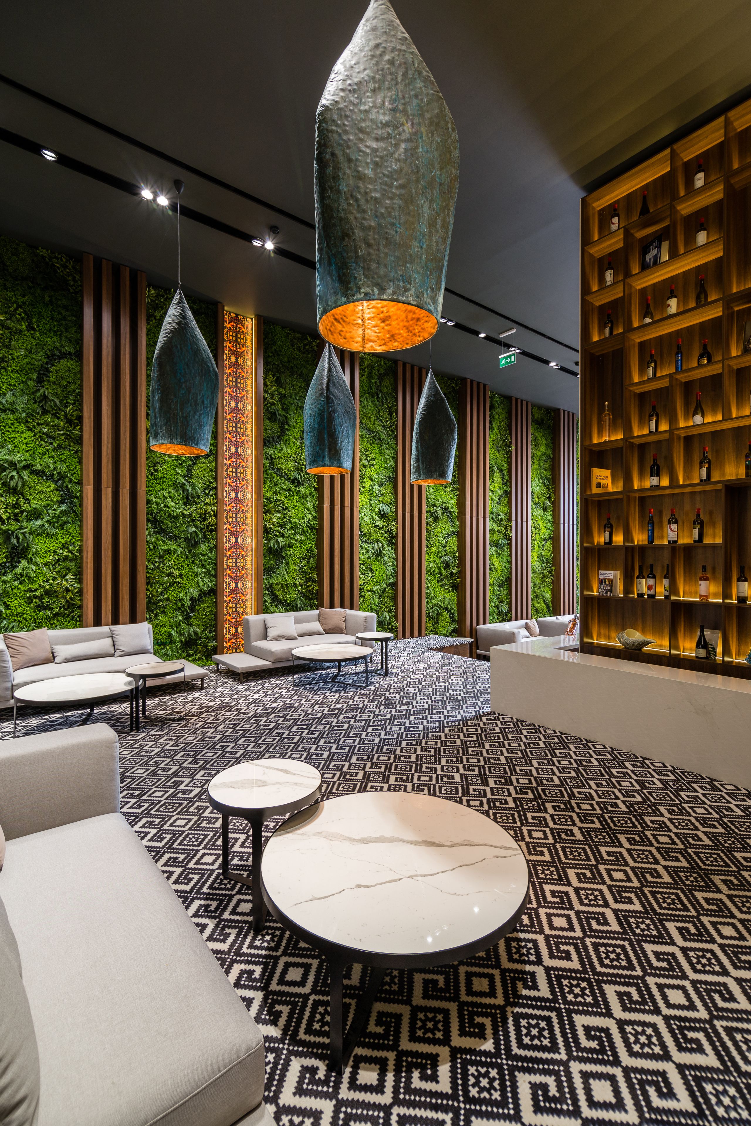 A modern lobby with a green wall, patterned carpet, and a bar area with shelves of bottles.