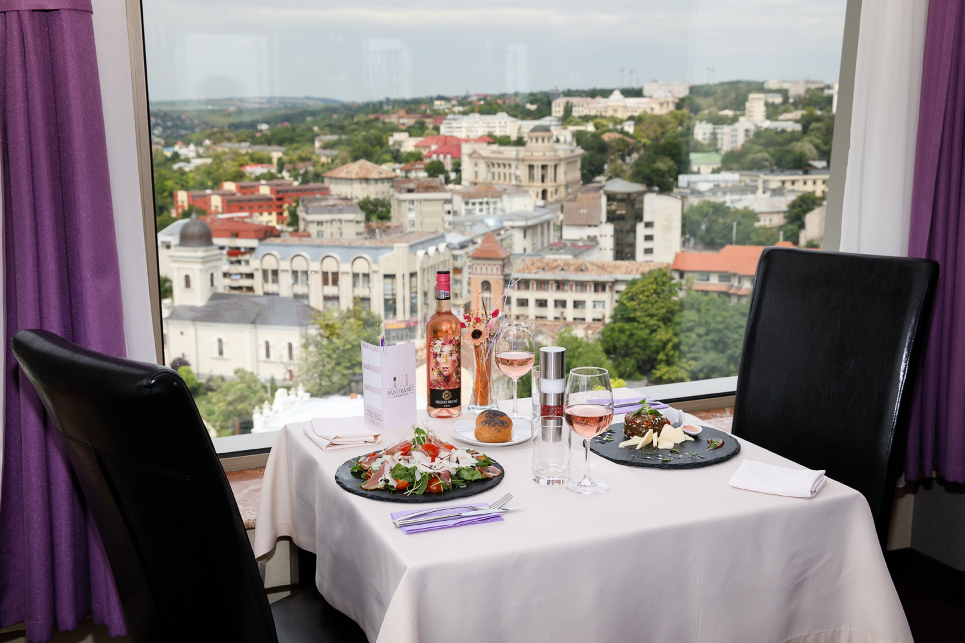 A dining table with a city view, a bottle of wine, and a glass of wine.
