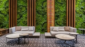 A modern lounge area with two sofas, a patterned rug, and a green wall with vertical wooden slats.