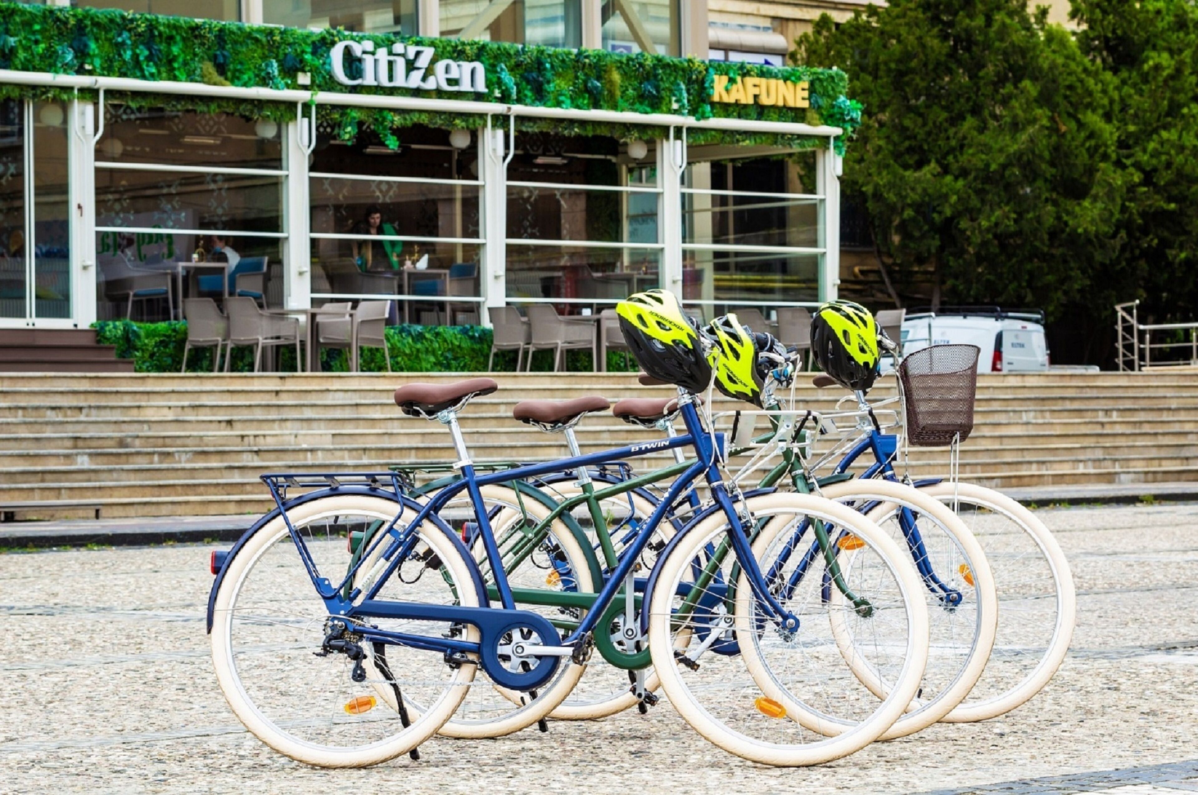 A bicycle rack with multiple bicycles parked in front of a restaurant named 'Citizen' with outdoor seating.
