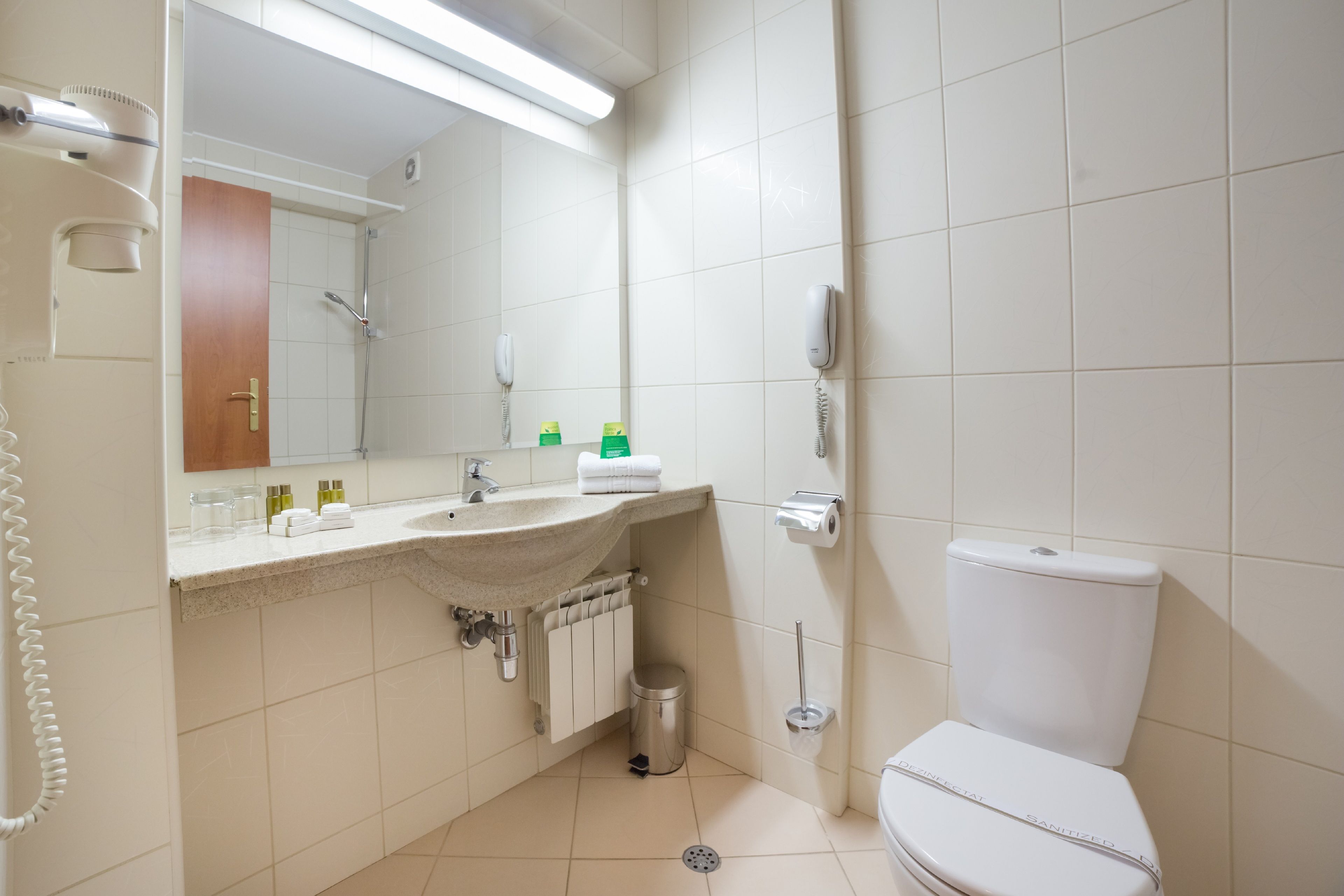 Une salle de bain équipée d’un lavabo, d’un miroir, de toilettes et d’une poubelle.