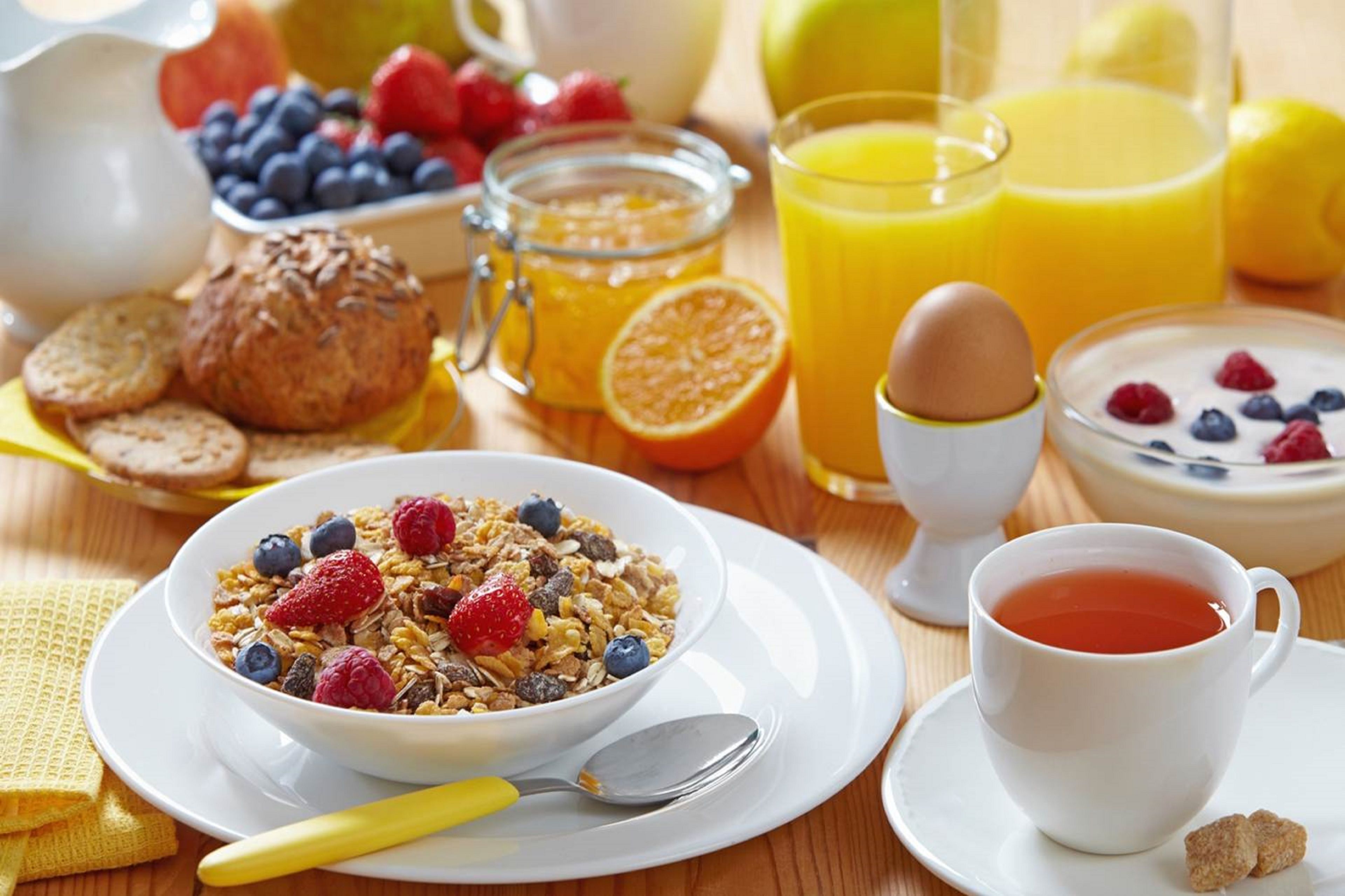 Desayuno con cereal, frutas, un muffin, un vaso de zumo de naranja, un vaso de leche y una taza de té.
