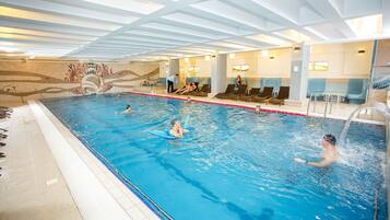 An indoor swimming pool with multiple lanes, lounge chairs, and a mural on the wall.