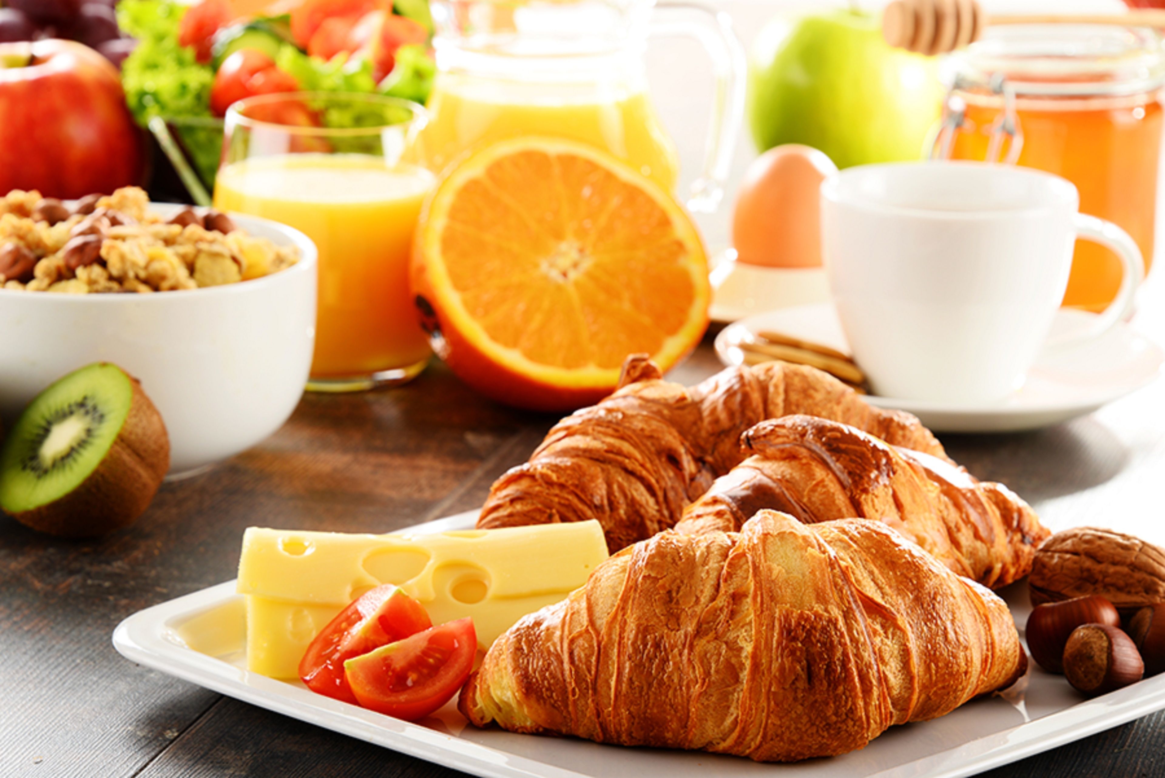 Disposição para o pequeno-almoço com croissants, queijo, tomates e um copo de sumo de laranja.