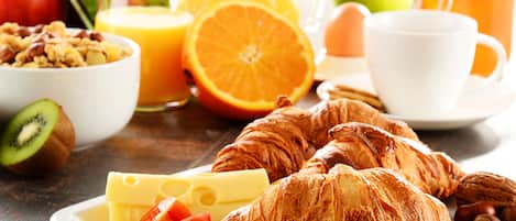 Disposição para o pequeno-almoço com croissants, queijo, tomates e um copo de sumo de laranja.