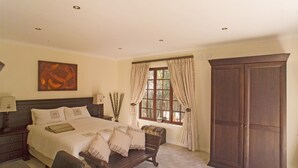 A bedroom with a large bed, a wooden wardrobe, a bench, and a window with curtains. - Three Palms Luxury Cottage (Cape Town)