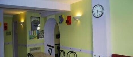 A dining area with tables and chairs, a clock on the wall, and a door leading to another room.