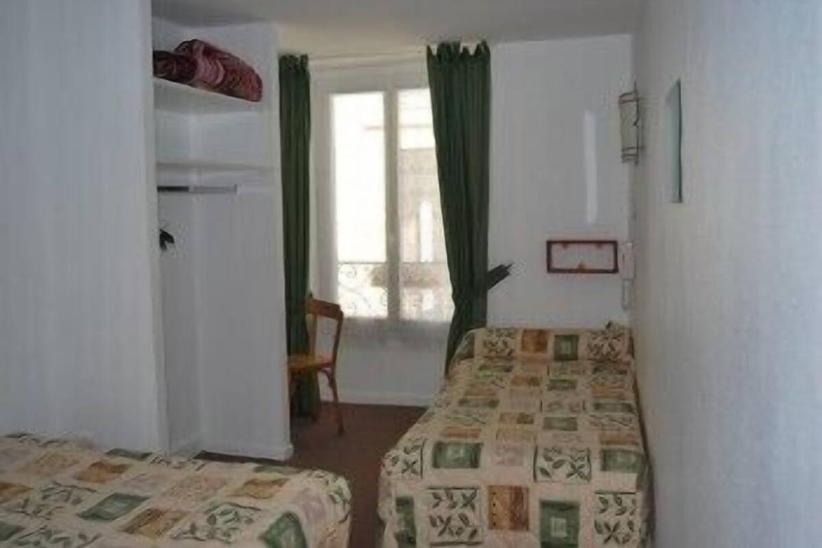 A room with two beds, a chair, a window with curtains, and a wall-mounted picture frame.