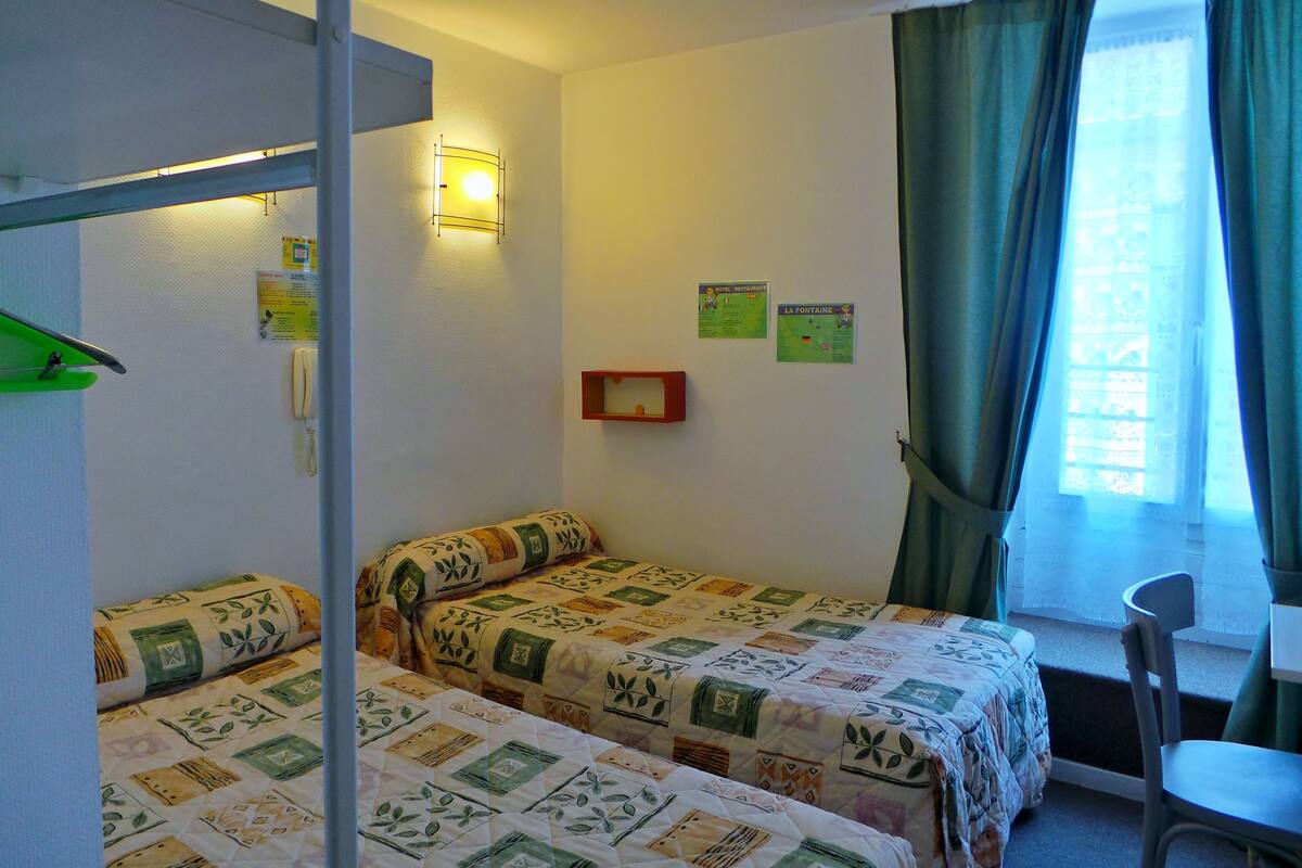 A room with two beds, a desk, a chair, a window with curtains, and wall-mounted signs.