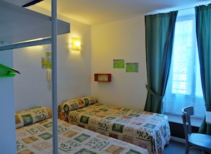 A room with two beds, a desk, a chair, a window with curtains, and wall-mounted signs. - Hôtel La Fontaine (Lourdes)
