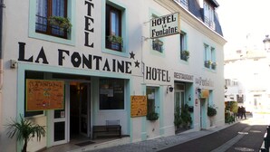 A building with signs reading "HOTEL LA FONTAIÊ" and "HOTEL RESTAURANT LA FONTAIÊ". There are potted plants on the windowsills and a bench outside. - Hôtel La Fontaine (Lourdes)