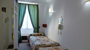 A room with two beds, a window with curtains, a wall-mounted light, and a small red object on the wall. - Hôtel La Fontaine (Lourdes)
