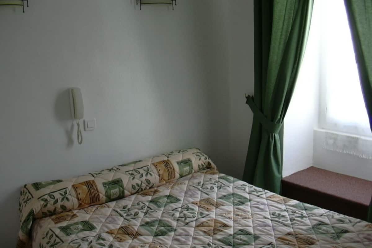 A bedroom with a bed, a bedside table, a telephone, and a window with curtains.