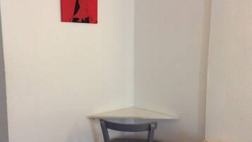 A corner room with a small table and a chair, a red artwork on the wall, and a white wall.