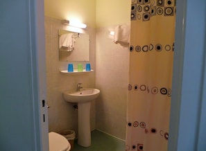 A small bathroom with a sink, mirror, and toilet. There is a towel rack above the sink and a shower curtain with a circular pattern. - Hôtel La Fontaine (Lourdes)