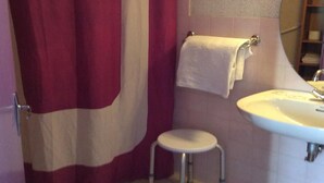 A bathroom with a shower curtain, a sink, and a small stool. - Hôtel La Fontaine (Lourdes)