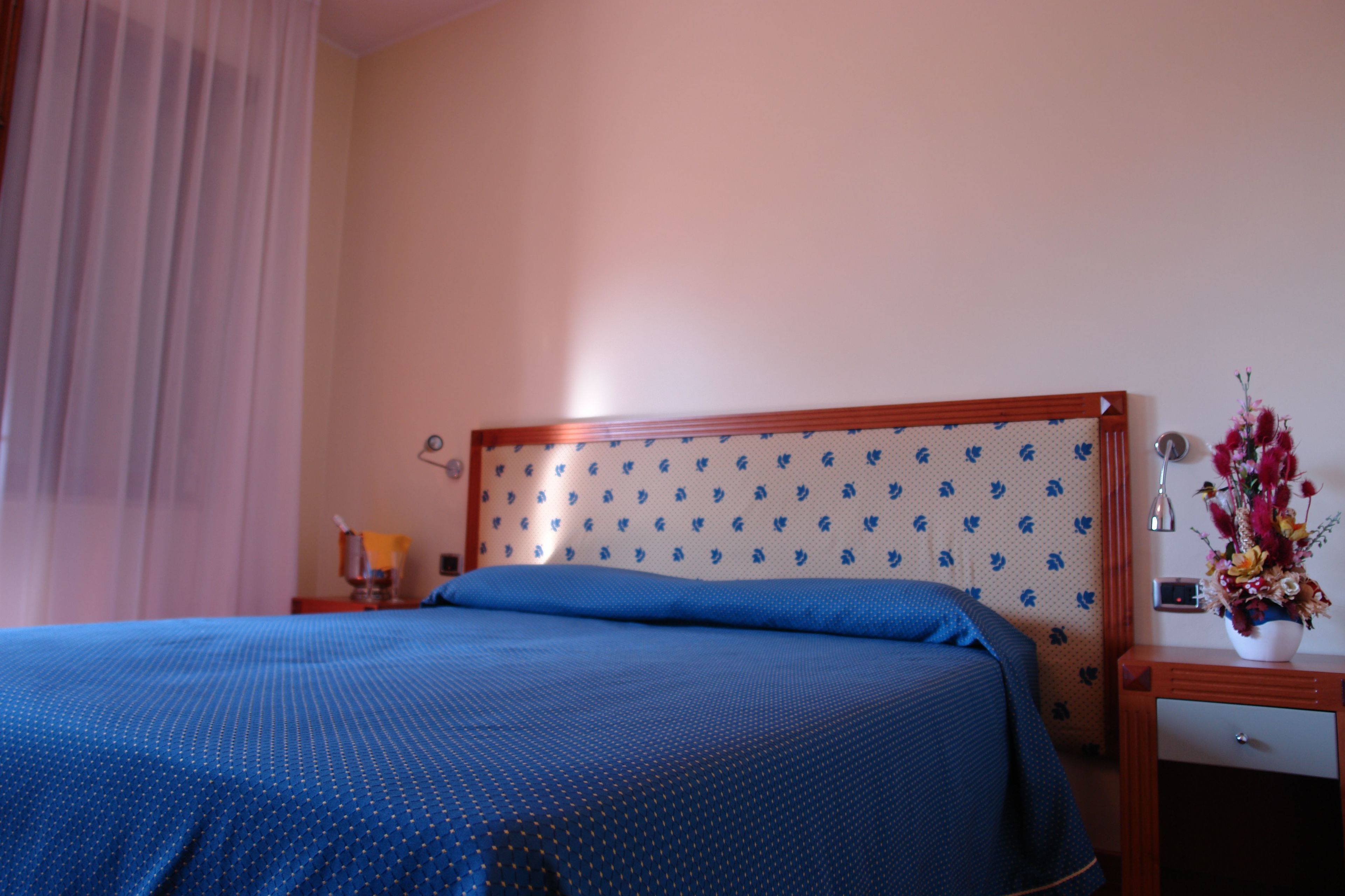 Ein Hotelzimmer mit Bett, Nachttisch, Lampe und einer Blumenvase.