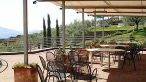 An outdoor patio with tables and chairs, a pergola, and a view of the countryside. - Il Castellaccio (Perugia)