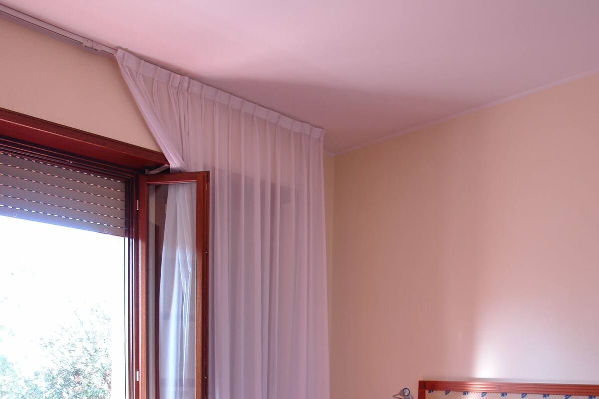 A hotel room with two beds, a wooden headboard, a nightstand with a lamp, and a window with curtains.