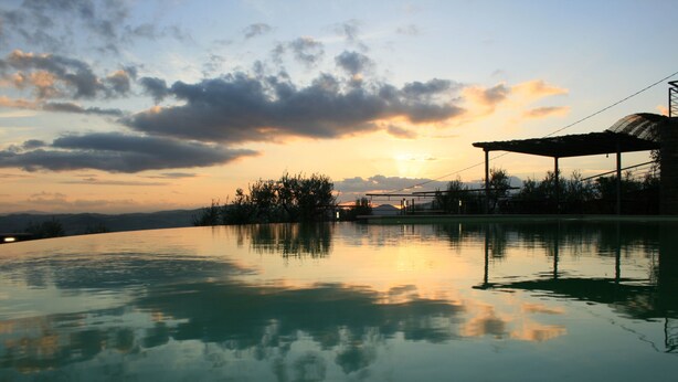 A serene outdoor pool area with a clear view of the sunset and surrounding landscape. - Il Castellaccio (Perugia)