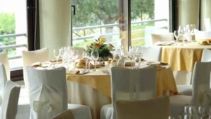 A restaurant with tables set for dining, large windows, and a view of greenery outside. - Il Castellaccio (Perugia)