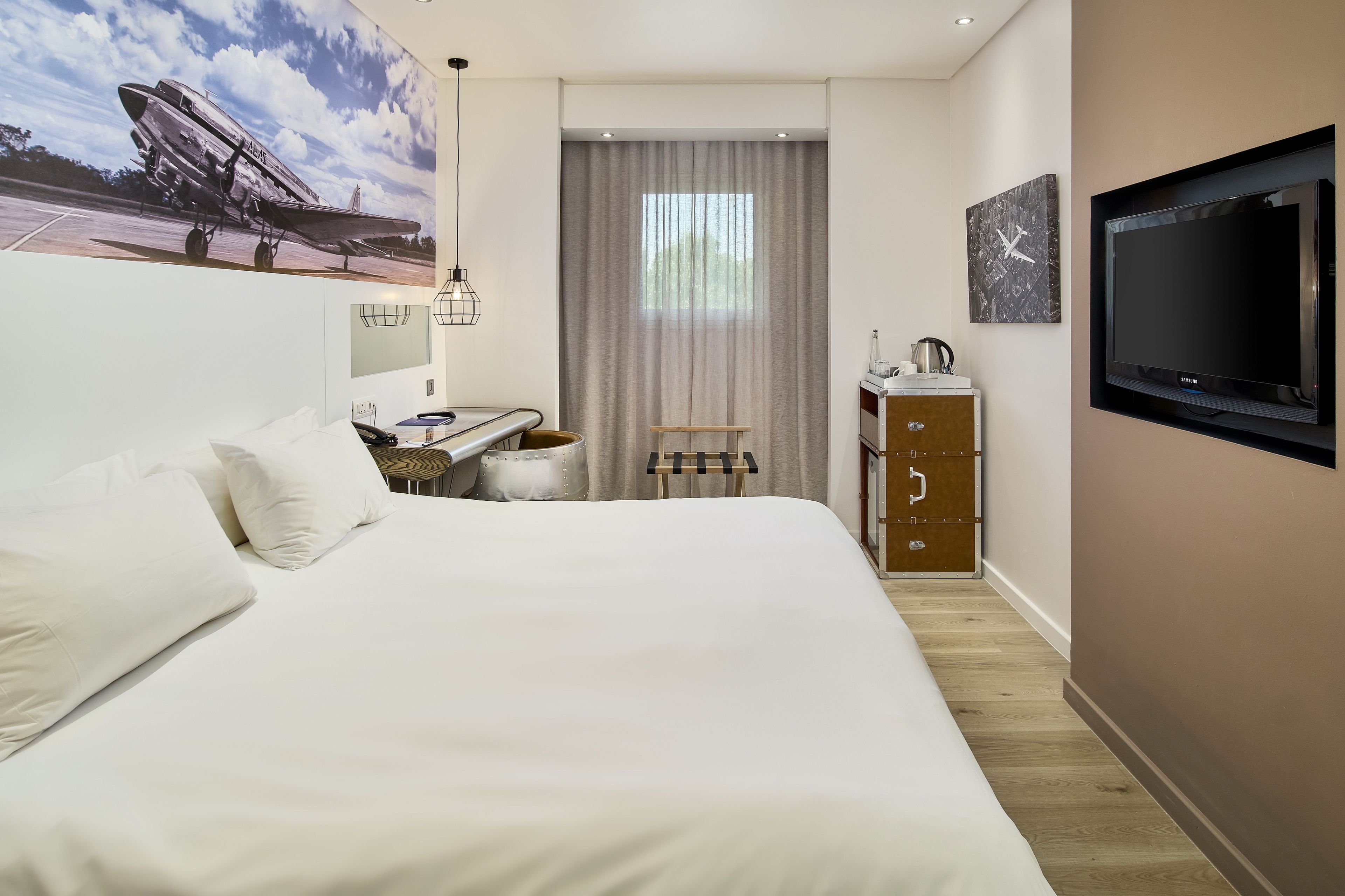 Una habitación de hotel con una cama grande, un escritorio con una silla, un televisor y un ventanal con cortinas.