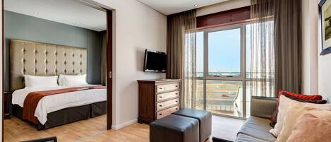 Habitación de hotel moderna con una cama grande, un sofá, un televisor y vistas al exterior.