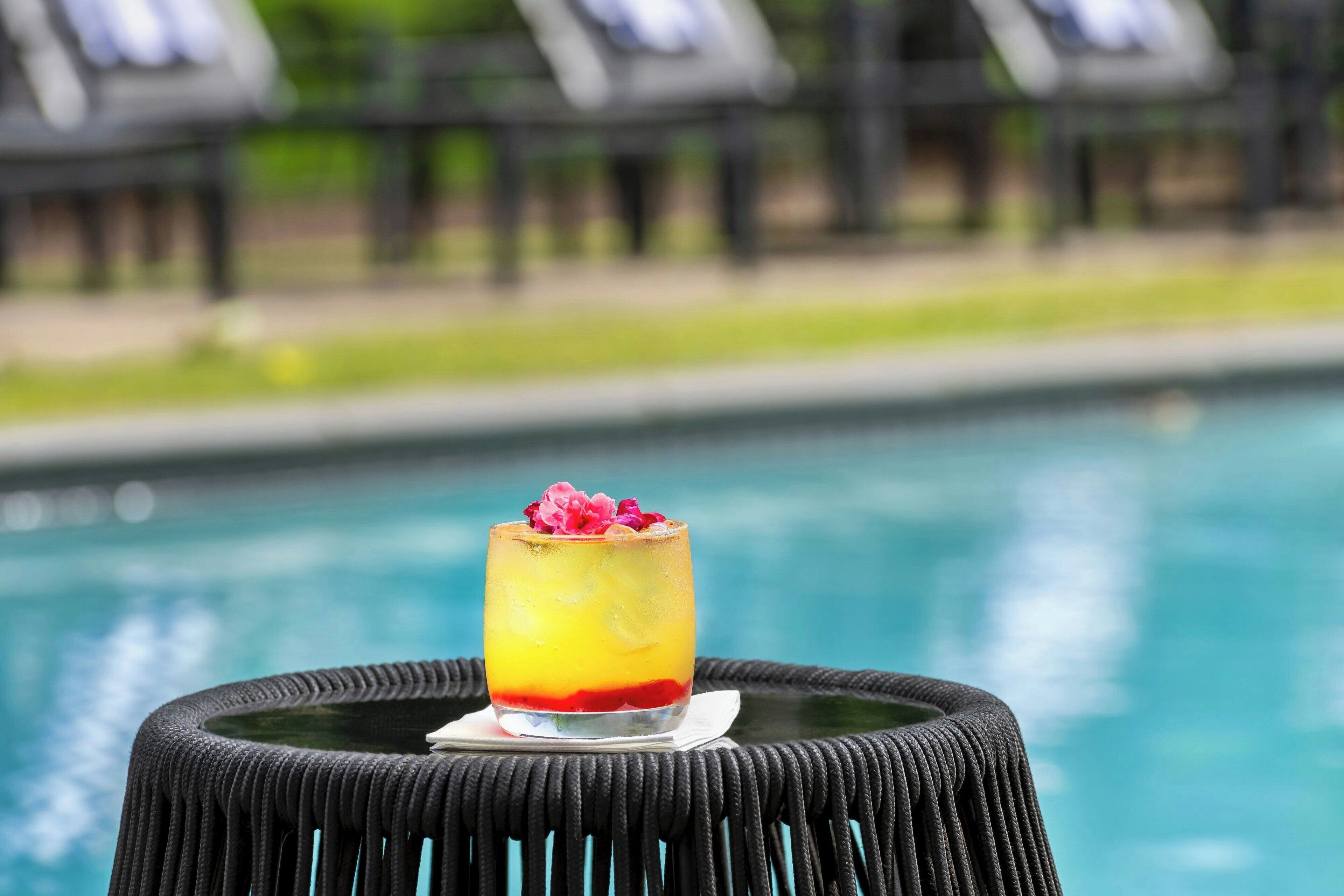 Un cocktail, une chaise en osier près d’une piscine, avec des chaises longues en arrière-plan.
