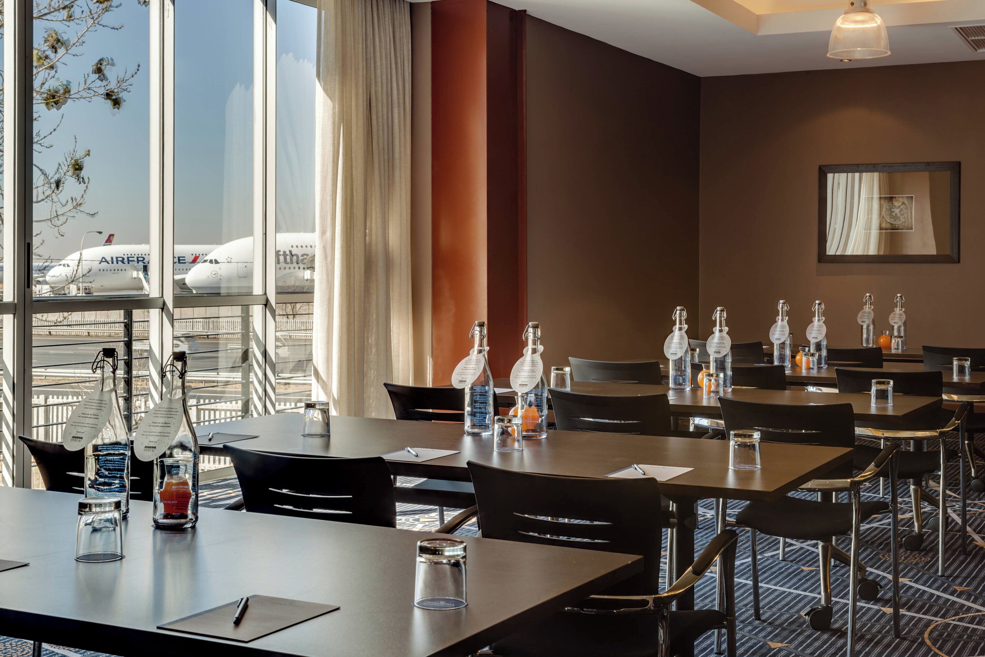 Une salle de conférence d’hôtel équipée de tables, de chaises et de bouteilles d’eau.