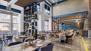 A modern dining area with high ceilings, exposed ductwork, and a large brick wall. - Protea Hotel by Marriott O.R. Tambo Airport (Kempton Park)