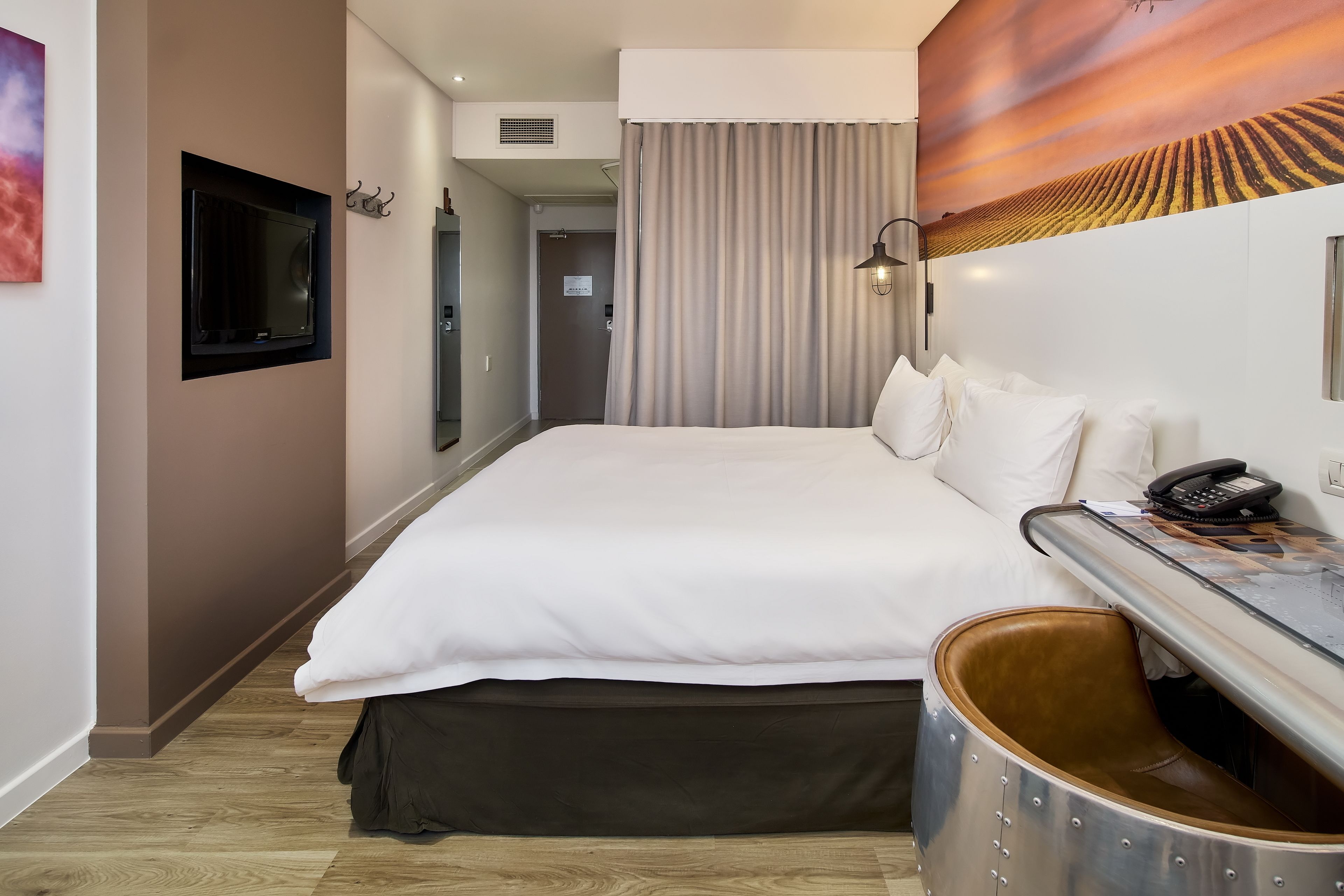 A hotel room with a large bed, a desk with a telephone, and a wall-mounted TV.