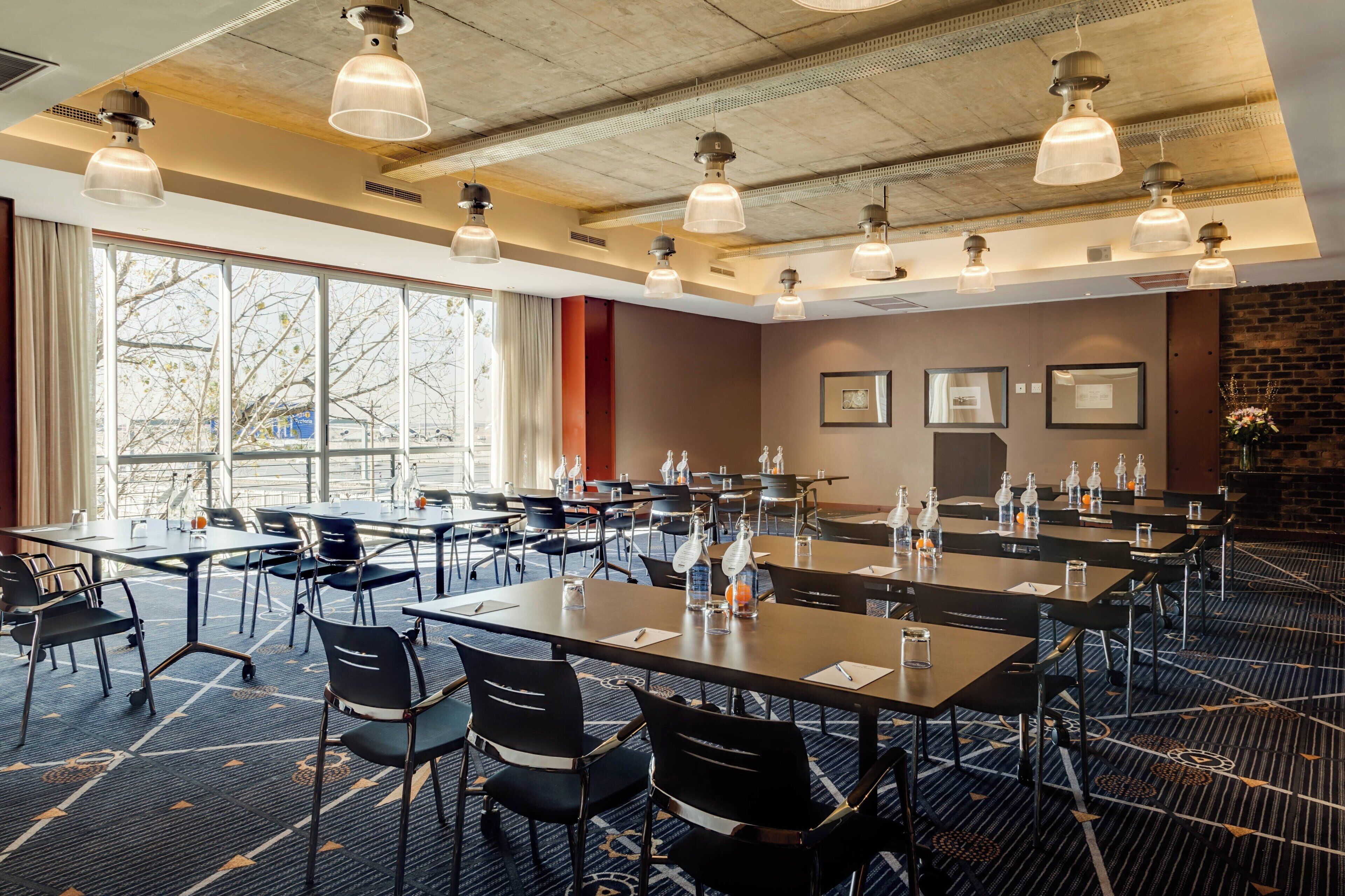 A conference room with multiple tables and chairs, large windows, and hanging pendant lights.