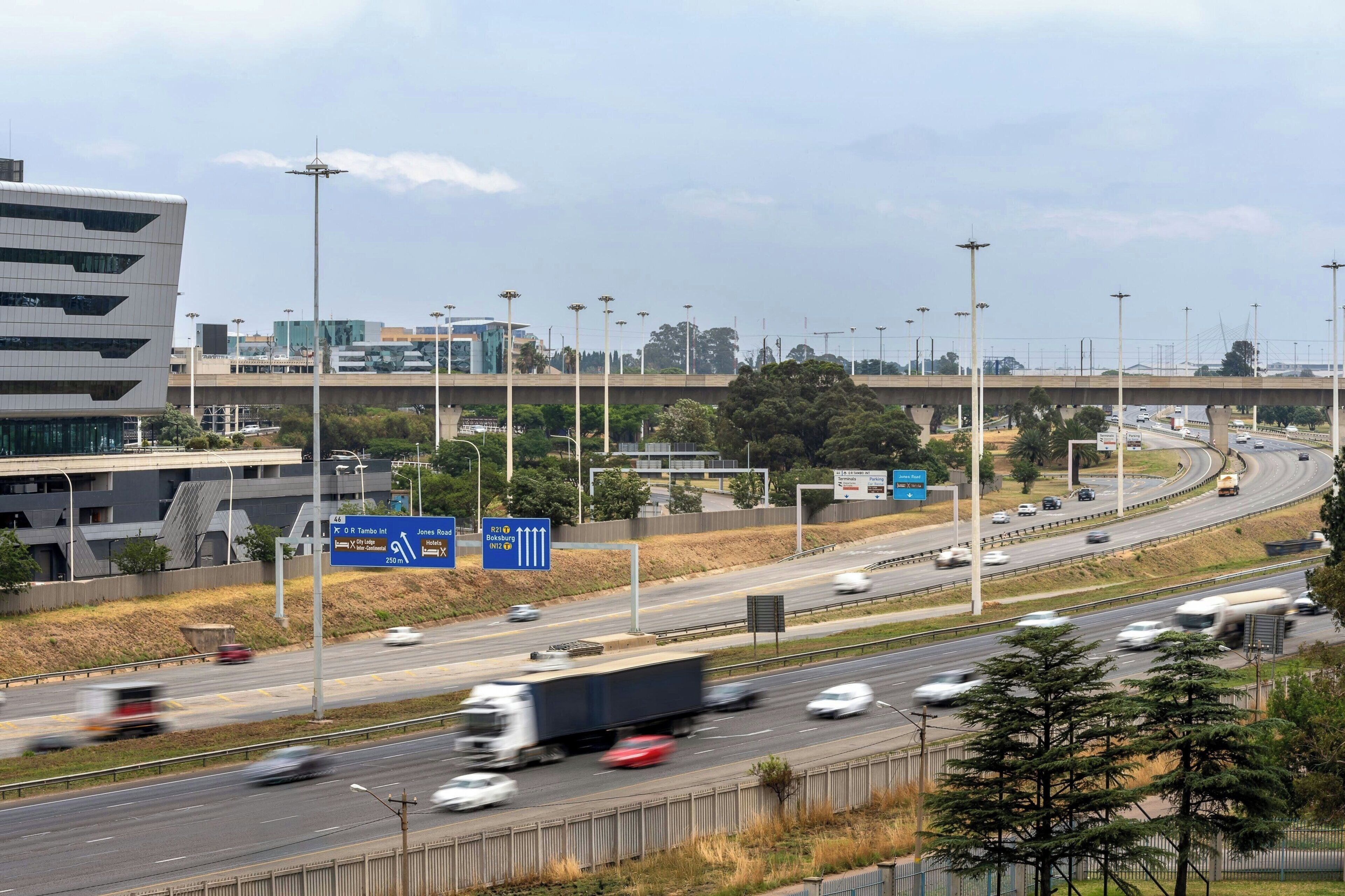 A multi-lane highway with vehicles, overhead signs, and modern buildings in the background.