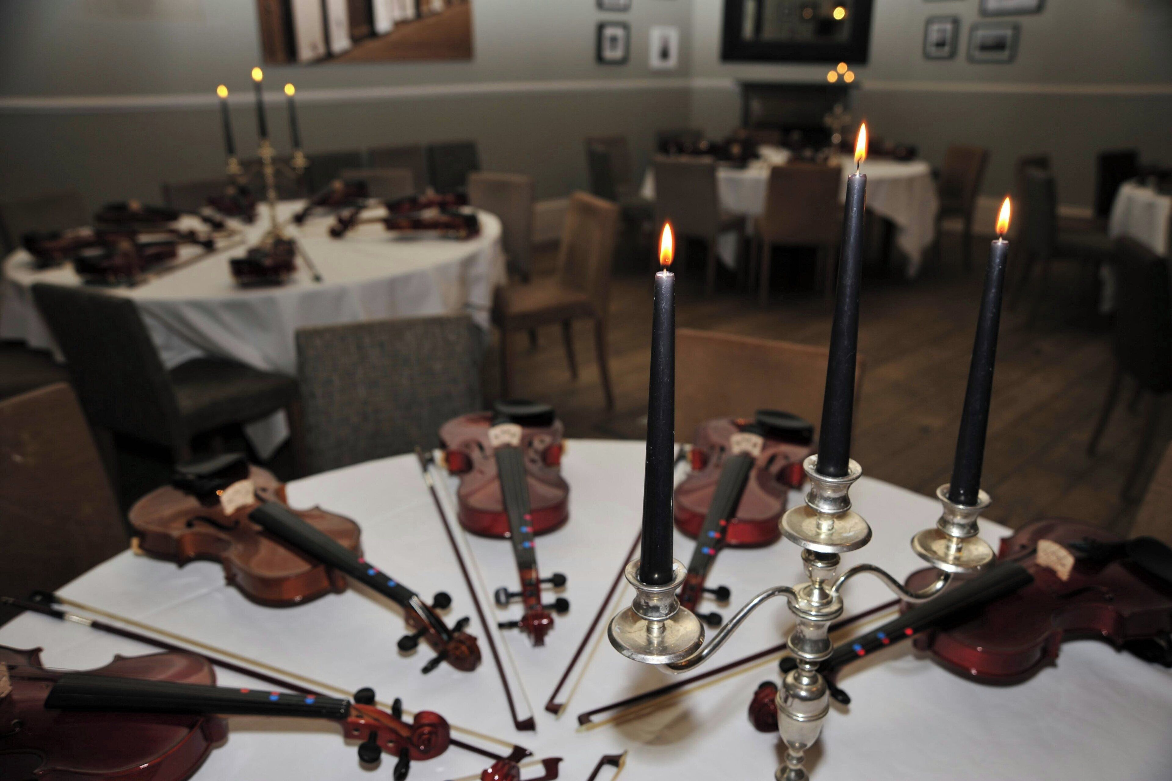A dining area with tables set for a meal, featuring violins and candles.