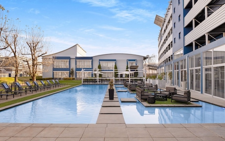 A swimming pool with lounge chairs and a sun deck, surrounded by modern buildings with large windows and balconies.