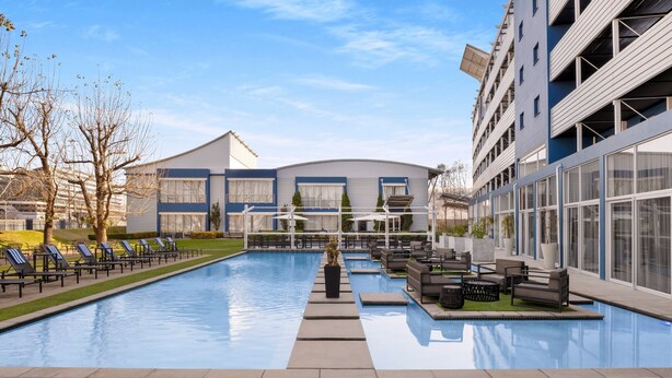 A swimming pool with lounge chairs and a sun deck, surrounded by modern buildings with large windows and balconies. - Protea Hotel by Marriott O.R. Tambo Airport (Kempton Park)