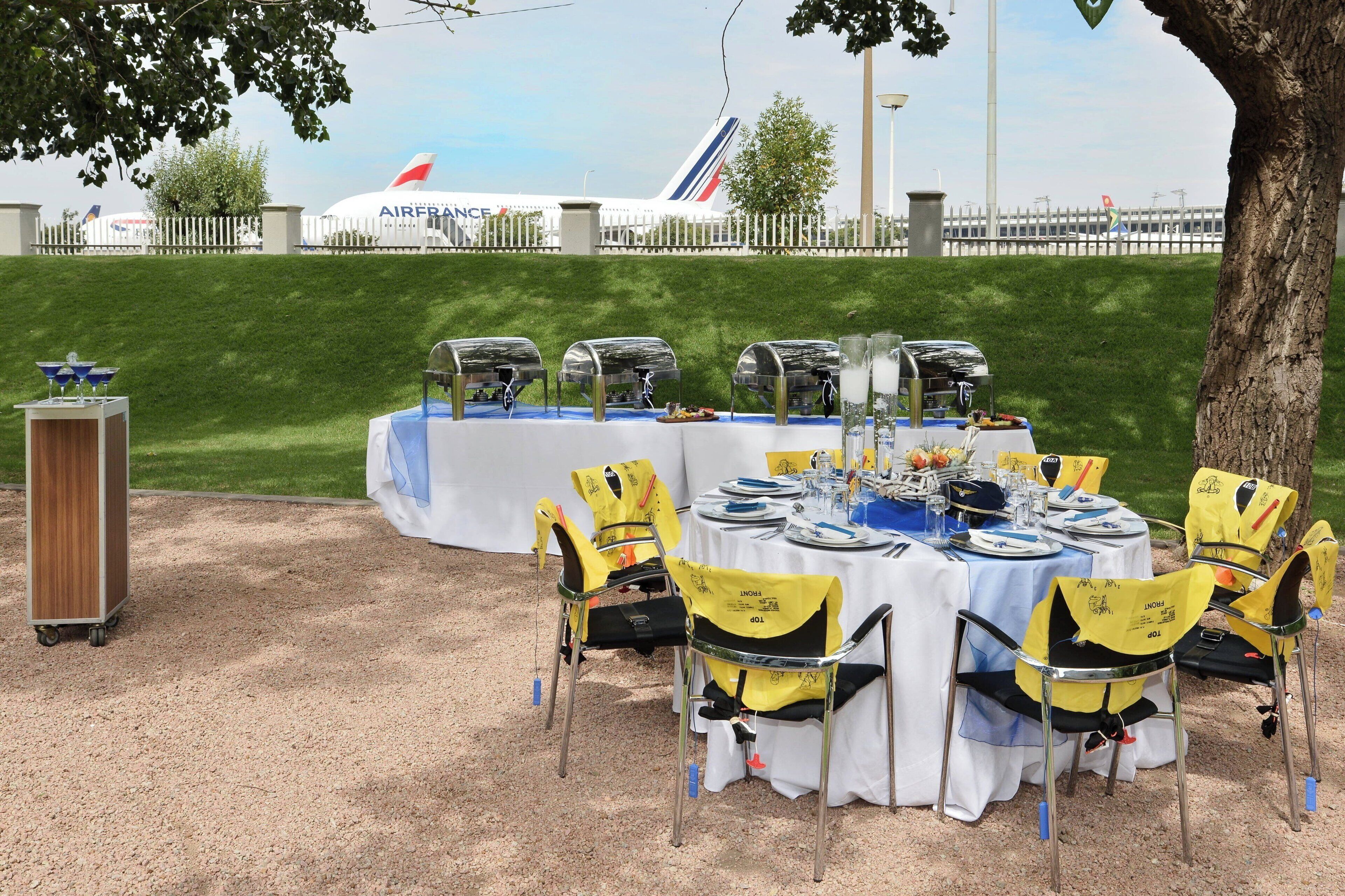 An outdoor dining setup with tables and chairs, a buffet area, and a large Air France airplane in the background.