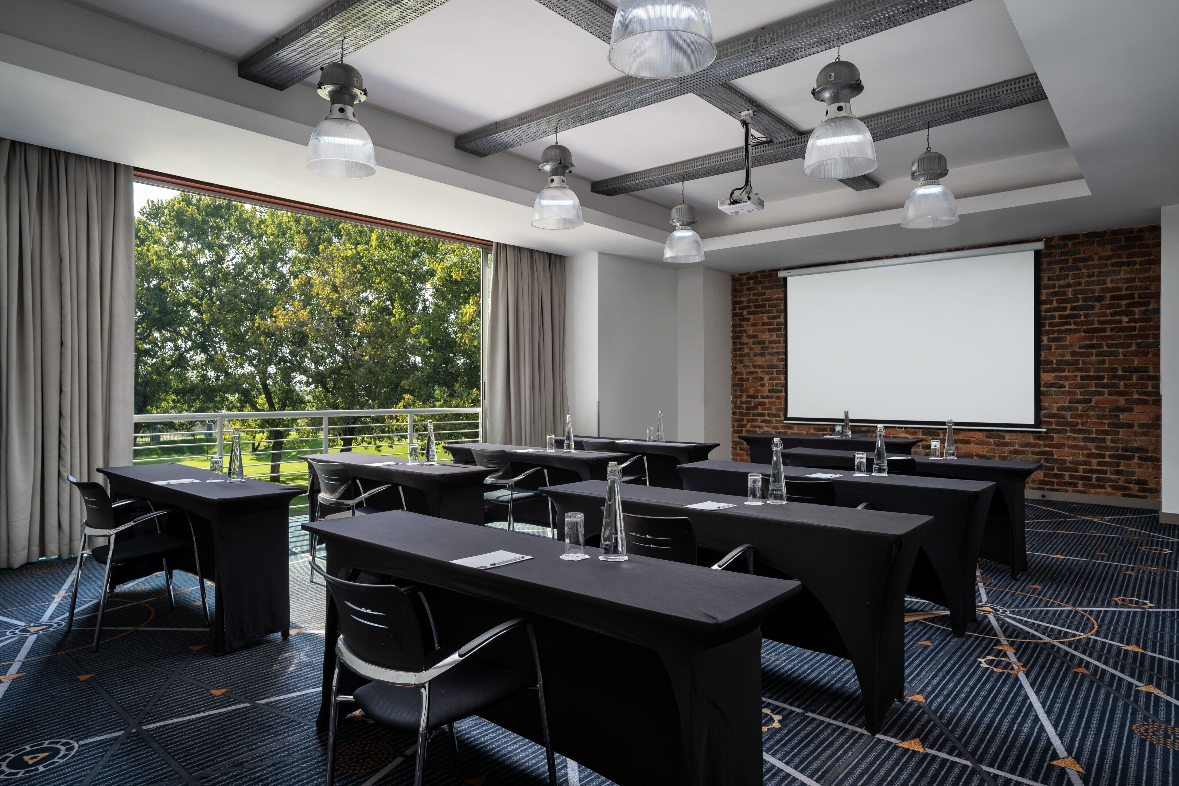 Une salle de conférence équipée de tables, de chaises, d’un écran de projection et offrant une vue sur les arbres grâce à de grandes fenêtres.