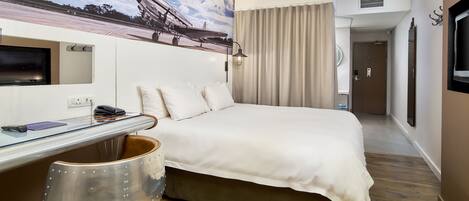 Habitación de hotel con cama, escritorio, silla, televisor y un cuadro de un avión en la pared.